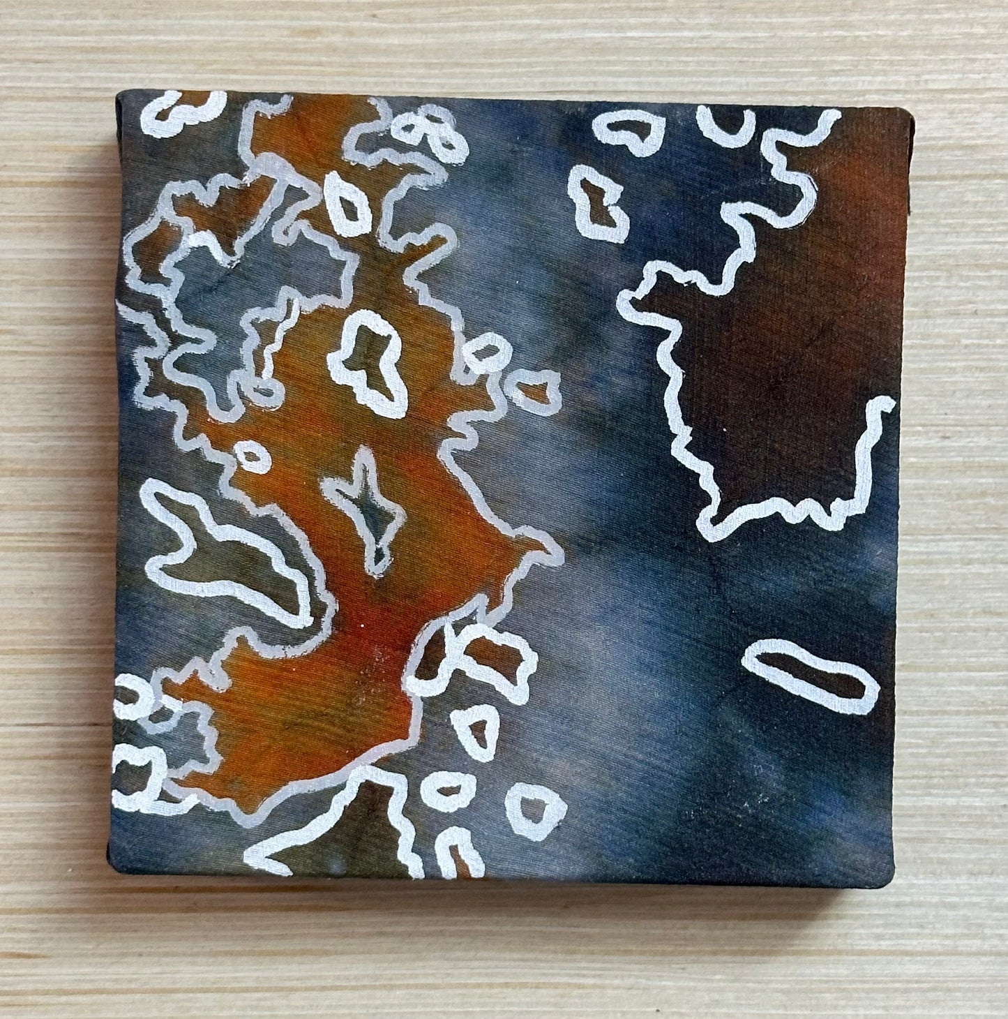 Square silk painting with white abstract design on a wooden surface