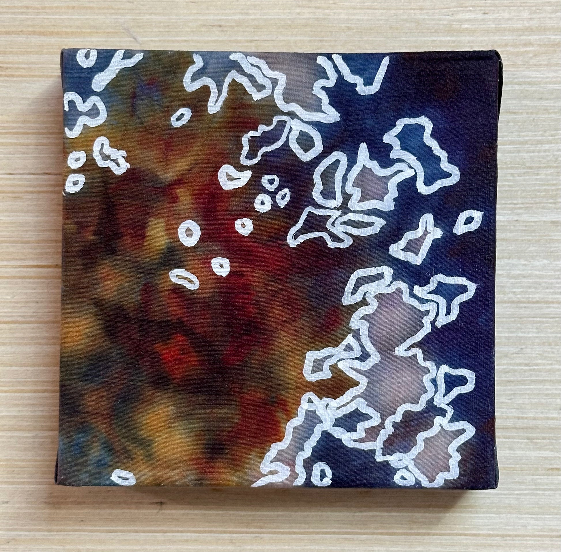 Square silk painting with white abstract design on a wooden surface