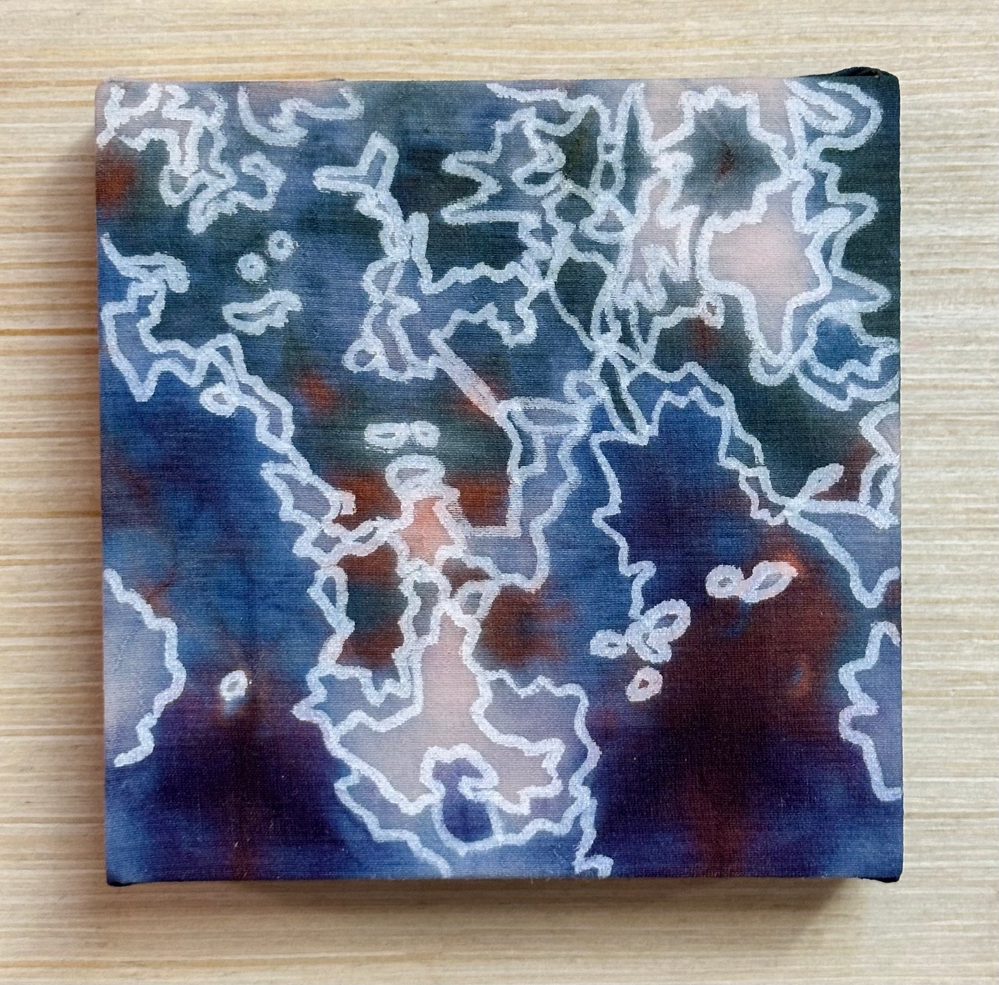 Square silk painting with white abstract design on a wooden surface