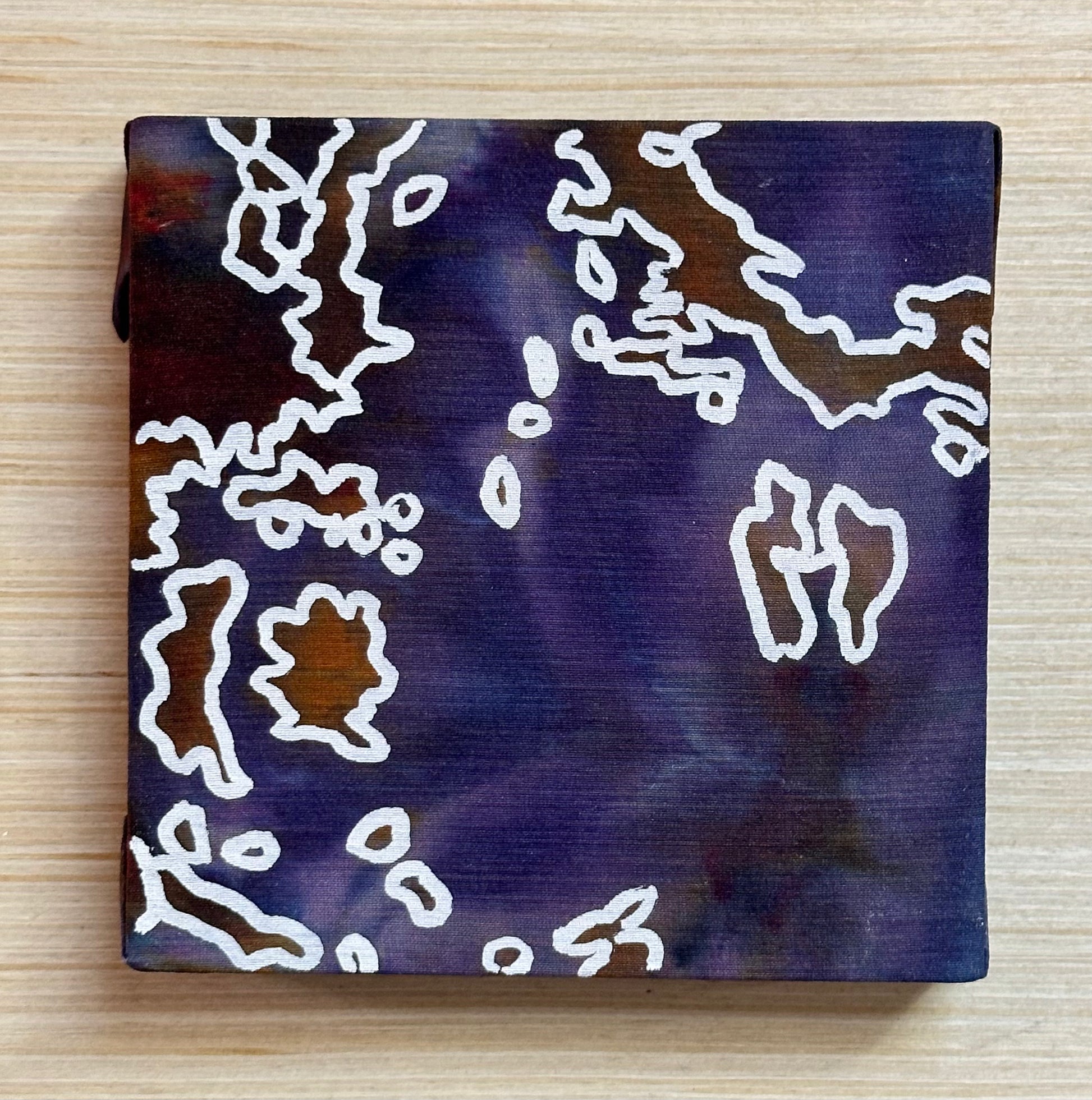 Square silk painting with white abstract design on a wooden surface