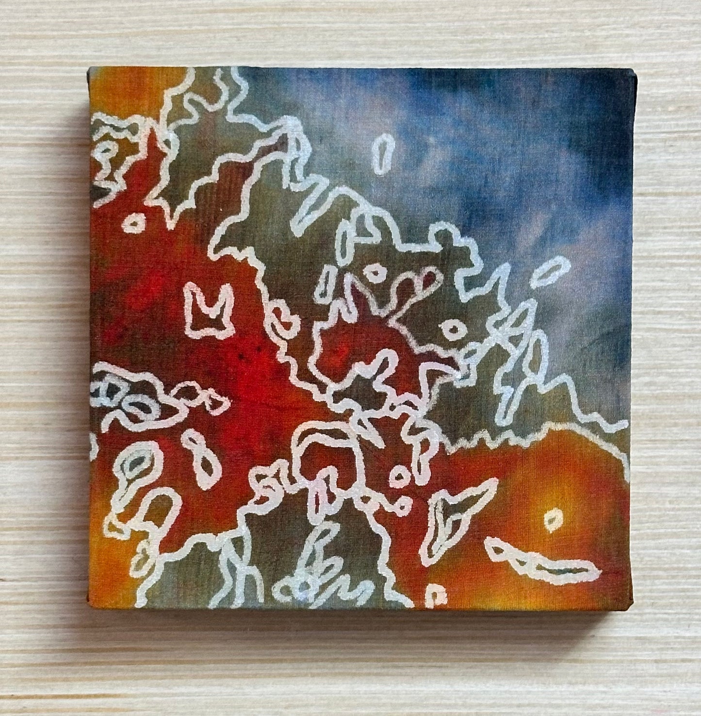 Square silk painting with white abstract design on a wooden surface