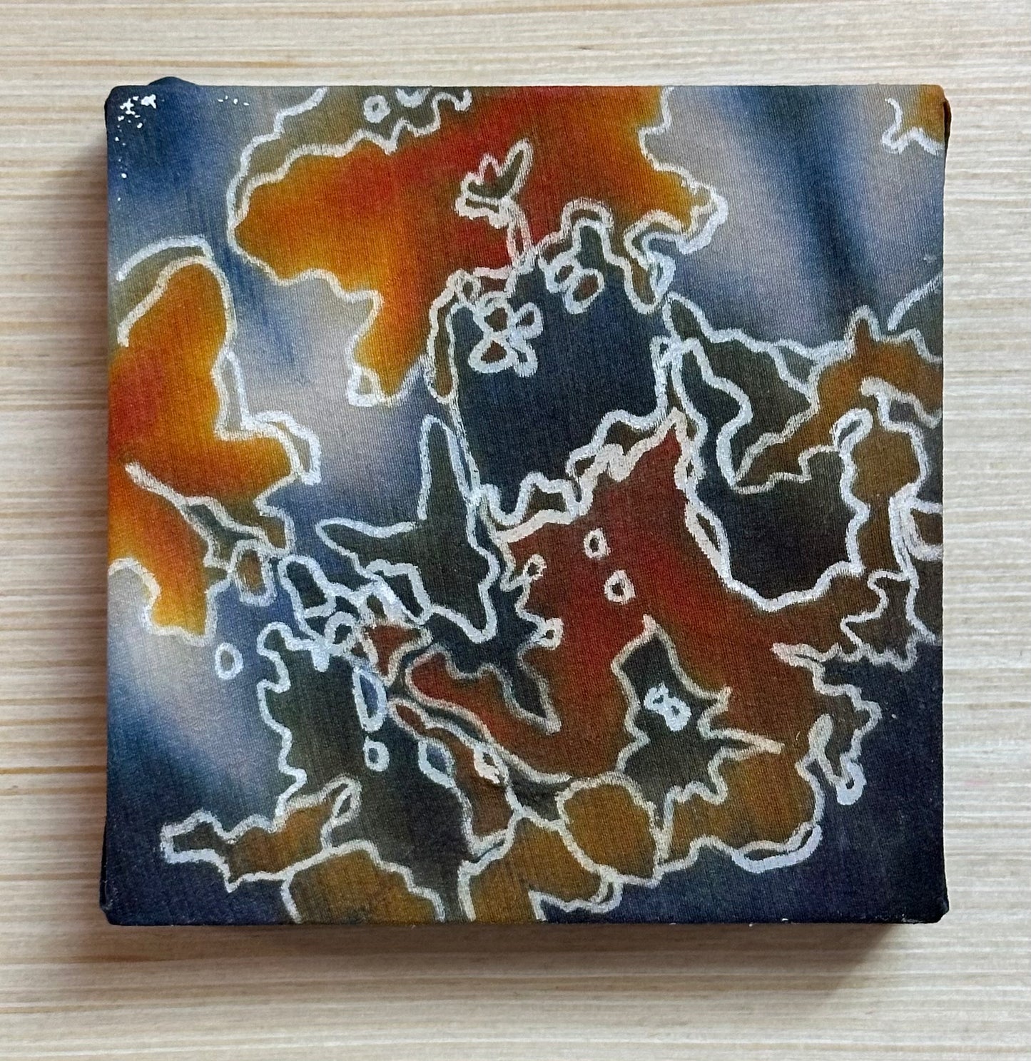 Square silk painting with white abstract design on a wooden surface