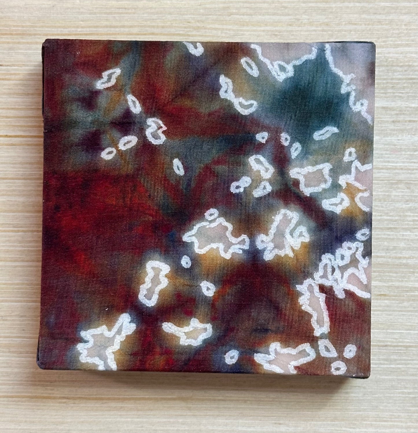Square silk painting with white abstract design on a wooden surface