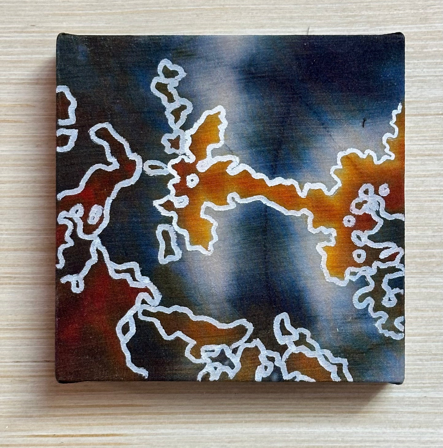 Square silk painting with white abstract design on a wooden surface