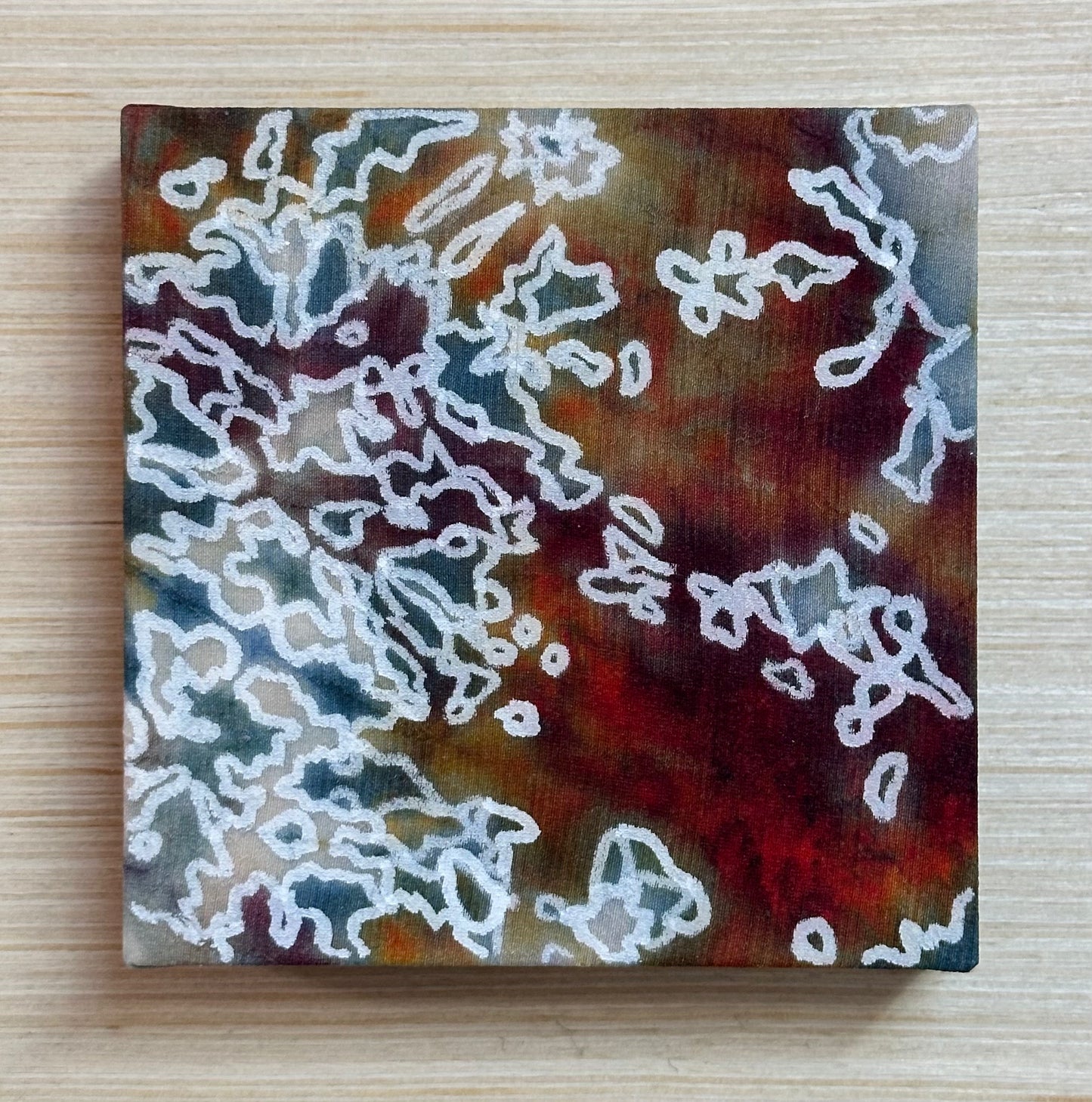 Square silk painting with white abstract design on a wooden surface