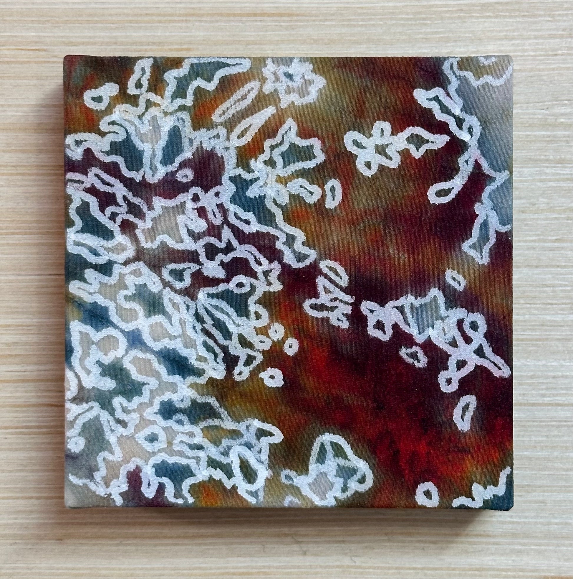 Square silk painting with white abstract design on a wooden surface