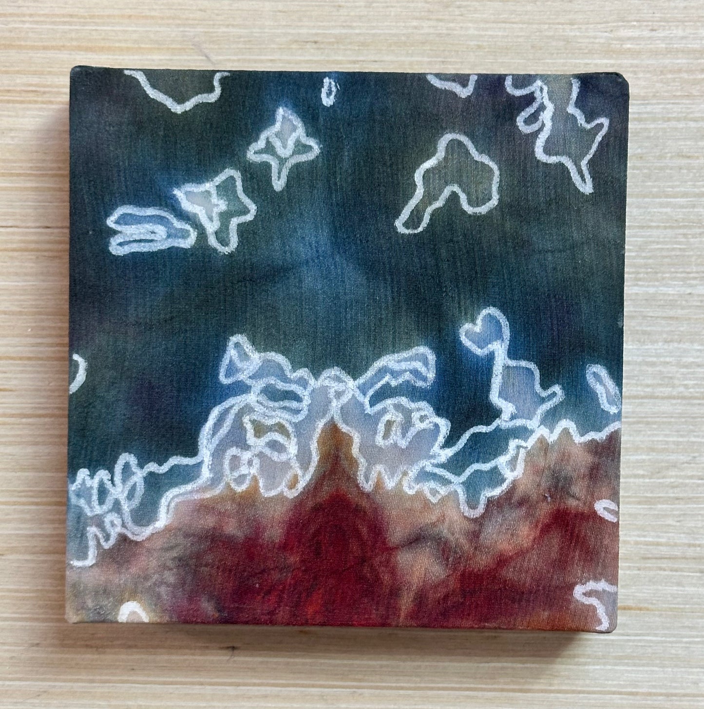 Square silk painting with white abstract design on a wooden surface