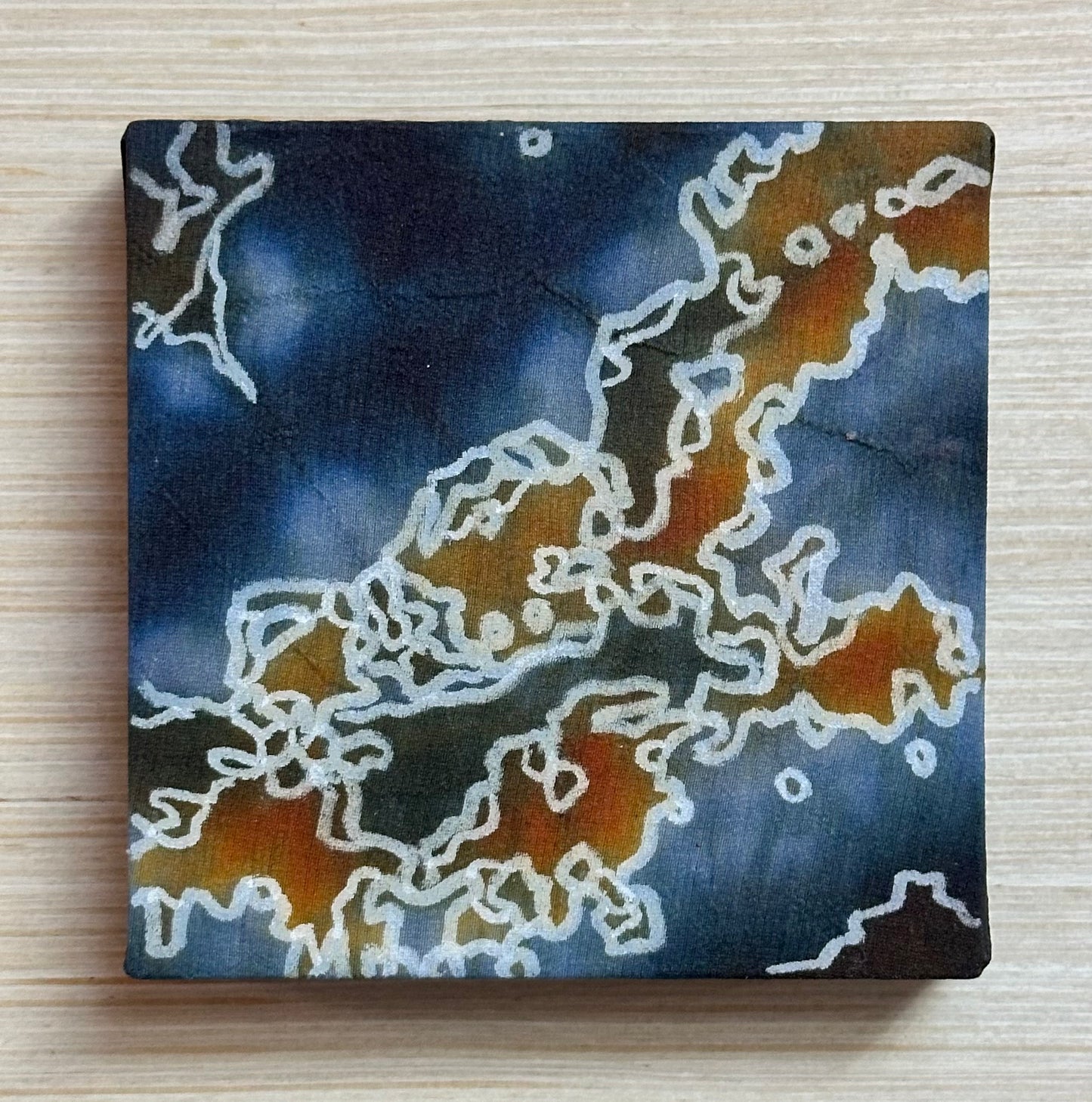 Square silk painting with white abstract design on a wooden surface
