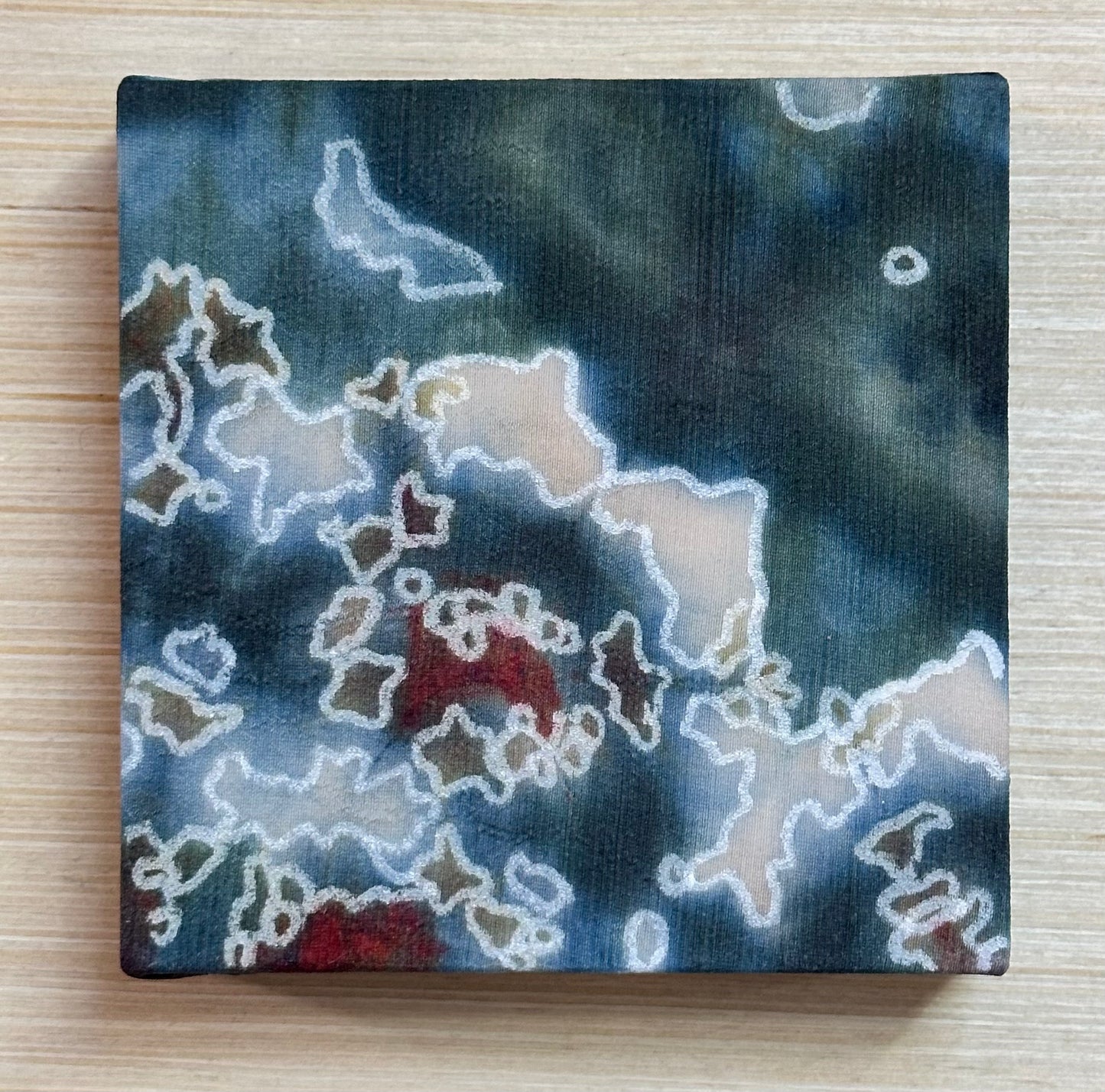 Square silk painting with white abstract design on a wooden surface