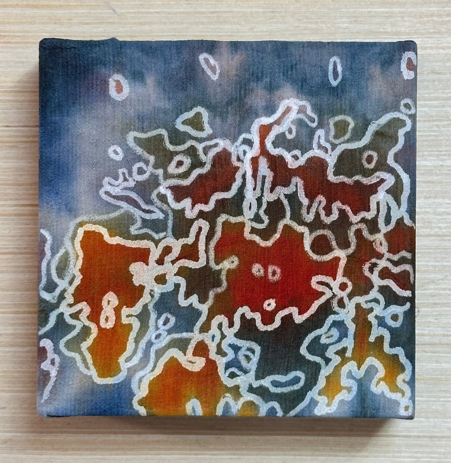 Square silk painting with white abstract design on a wooden surface