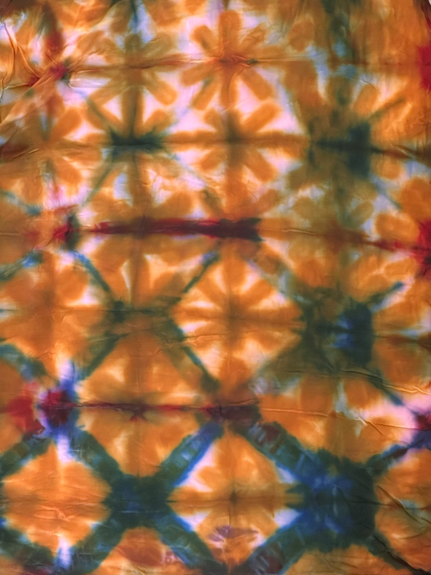 A close-up of a tie-dye fabric with a repeating geometric starburst pattern in orange, green, blue, and white.