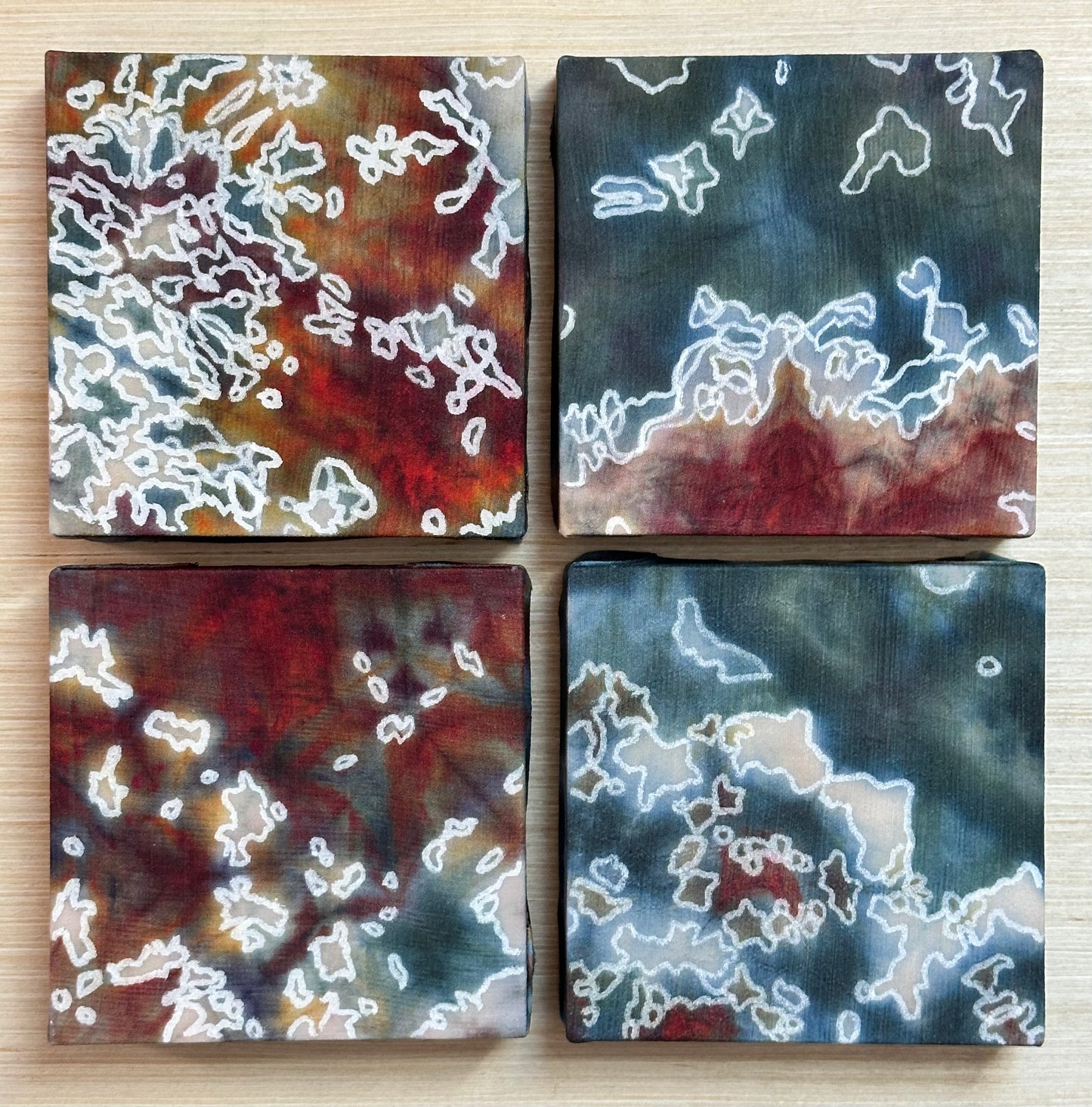 Four square silk paintings with white abstract design on a wooden surface
